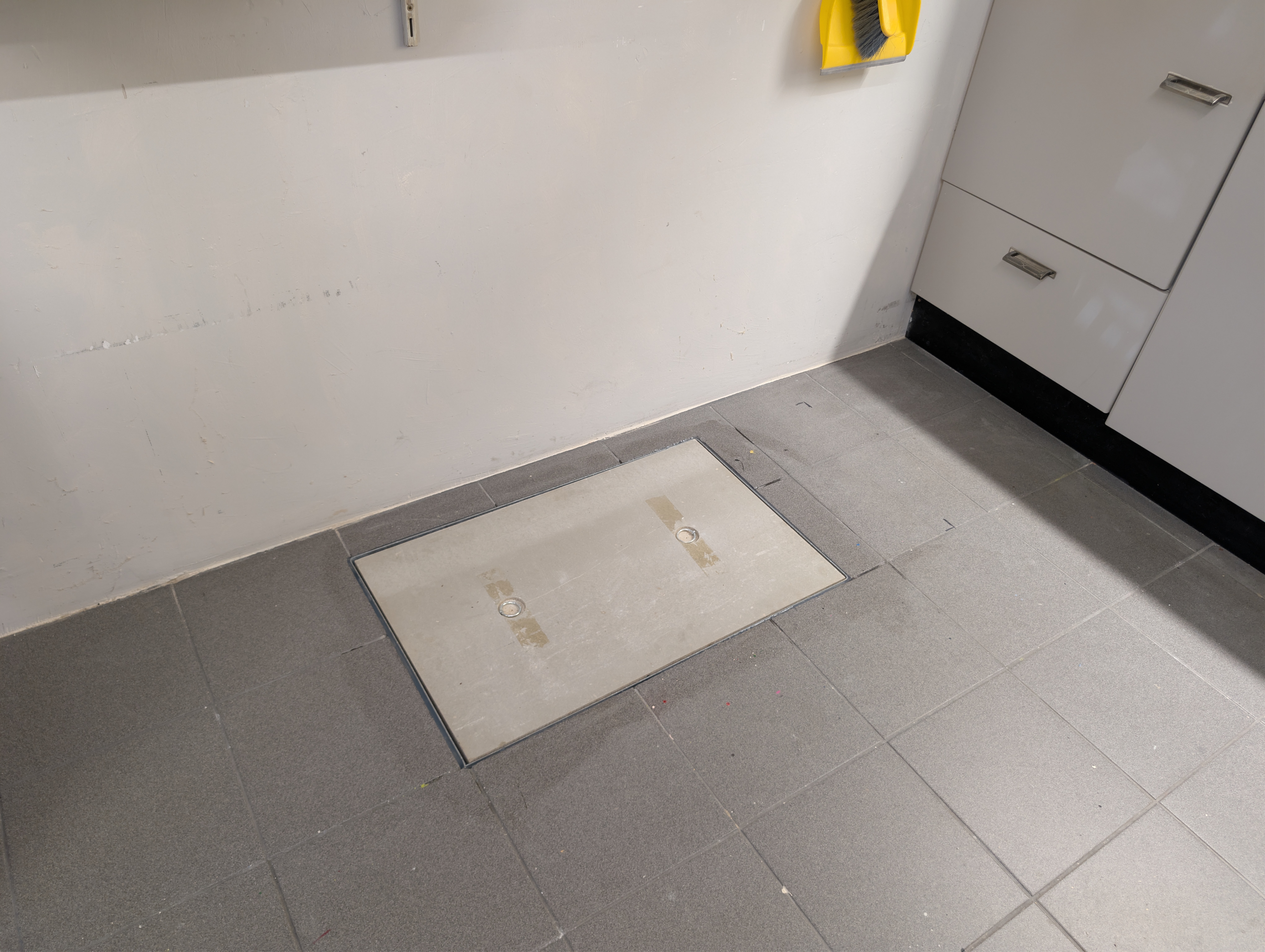 Gesloten kruipluik met metalen omranding in een grijze tegelvloer